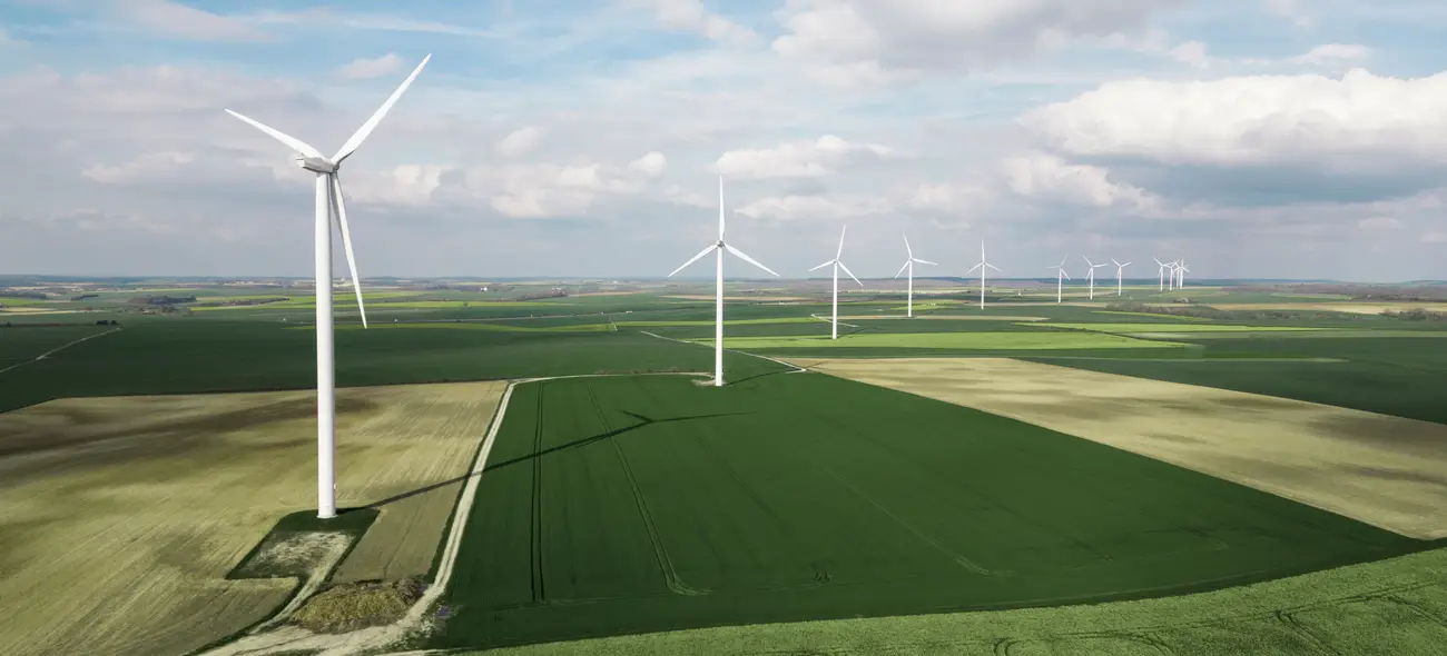 Windkraftanlagen auf einem weiten grünen Feld unter wolkigem Himmel.