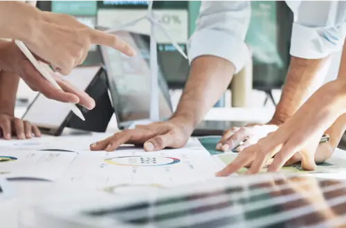 Hände mehrerer Personen arbeiten an Plänen und Diagrammen zu Windenergieprojekten im Büro.