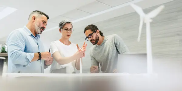 Team von drei Personen bespricht ein Windradmodell im Büro.